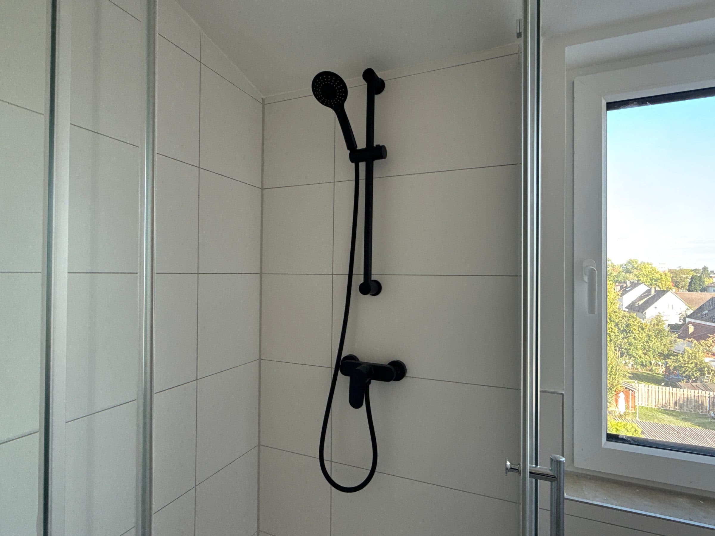 Dusche mit schwarzer Armatur neben dem Badfenster