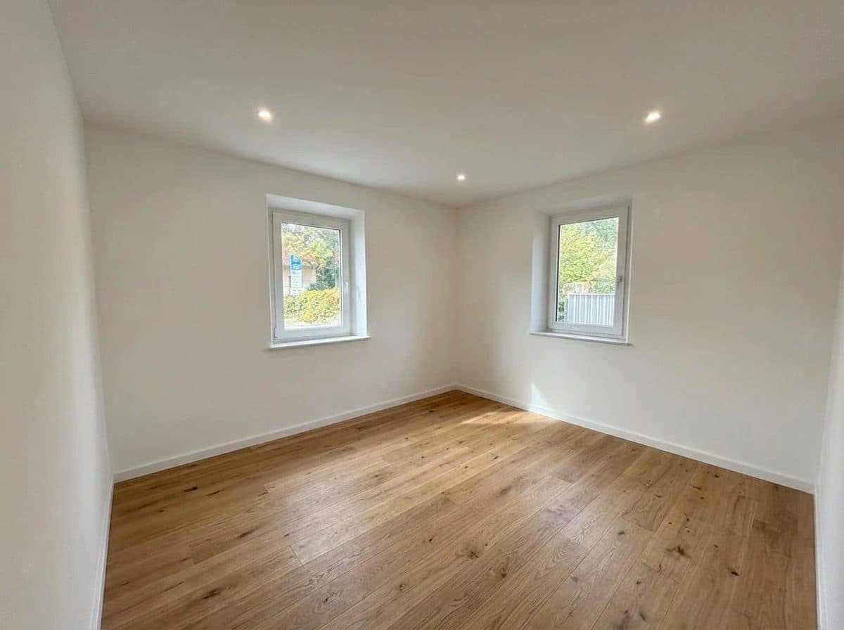 Wohnung 1: helles Zimmer mit zwei Fenstern und Holzboden